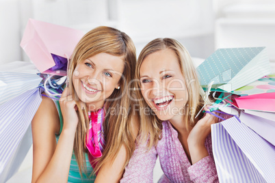 Delighted two women holding shopping bags smiling at the camera