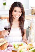 Positive asian woman holding a glass of wine having dinner