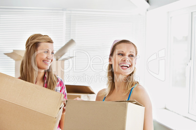 Laughing female friends holding boxes after moving