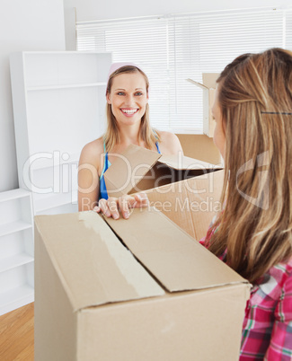 Two radiant female friends holding boxes after moving