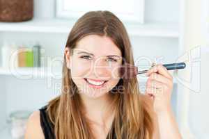 Smiling caucasian woman putting powder on her face smiling at th