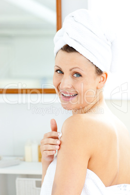 Delighted young woman putting cream on her body looking at the c