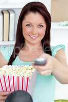 Cute caucasian woman holding a remote and popcorn looking at the