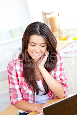 Glowing asian woman using her laptop sitting sitting in the kitc