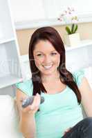 Bright caucasian woman holding a remote sitting on a sofa