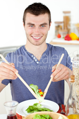 Handsome young man eating a salad smiling at the camera