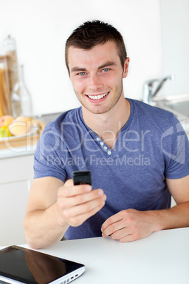 Lively young man sending a text smiling at the camera