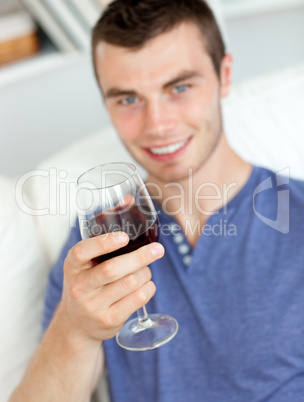 Charismatic young man holding a glass of wine sitting on a sofa