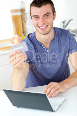 Charismatic young man holding a card using his laptop in the kit