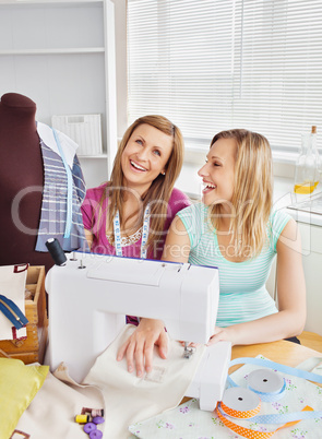Laughing female friends sewing clothes together at home