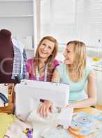 Laughing female friends sewing clothes together at home