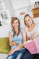 Two attractive female friends watching televison on the sofa eat
