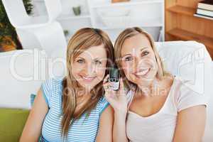 Two smiling women using a cellphone at home