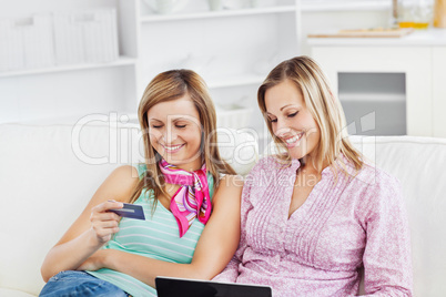 Two smiling women using a laptop and holding a card on the sofa