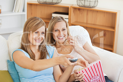 Two bright female friends watching televison on the sofa eating