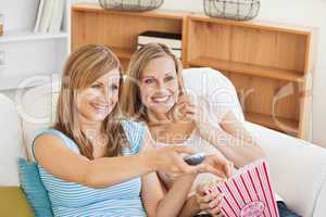 Two bright female friends watching televison on the sofa eating