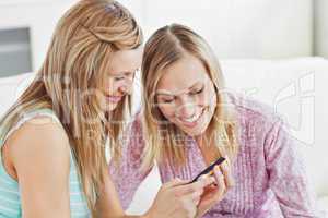 Delighted female friends using a cellphone at home