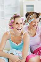 Female friends with hair rollers watching televison on the sofa