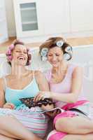 Delighted female friends with hair rollers eating chocolate read