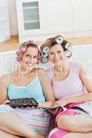 Smiling female friends with hair rollers eating chocolate readin