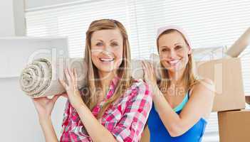 Two cute women carrying a carpet at home