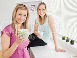 Portrait of two happy women holding cups of coffee at home