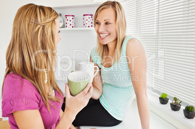 Portrait of two smiling women holding cups of coffee at home