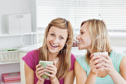 Positive female friends holding a cup of coffee at home