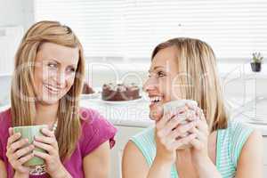 Delighted female friends holding a cup of coffee at home