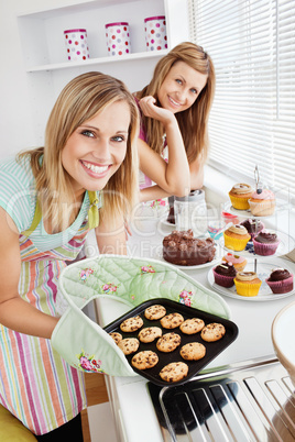 Happy female friends holding cookies in the kitchen