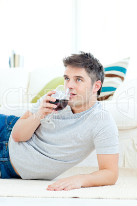 Positive young man drinking wine in the living-room