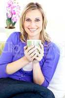 Caucasian blond woman enjoying her coffee sitting on the sofa