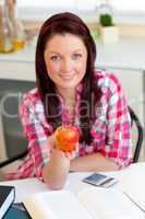 Serious caucasian woman holding an apple sitting in the kitchen