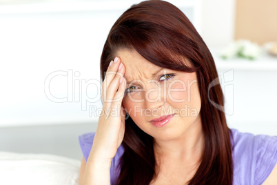 Cute woman with a headache sitting on a sofa at home