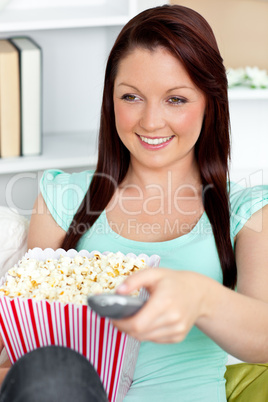 Charming caucasian woman holding a remote and popcorn in the liv
