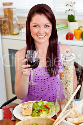 Charming woman eating her meal holding a glass of wine at home