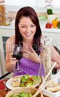 Delighted woman eating her meal holding a glass of wine at home