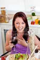 Cheerful woman eating her meal holding a glass of wine at home