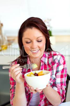 Merry woman eating a fruit salad for breakfast in the kitchen
