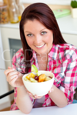 Glowing woman eating a fruit salad for breakfast in the kitchen