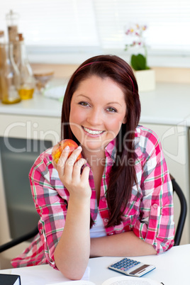 Delighted caucasian woman holding an apple sitting in the kitche
