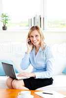 Radiant businesswoman using her phone and laptop in her living-r