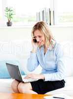 Glowing businesswoman using her phone and laptop in her living-r