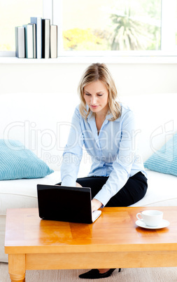 Glowing businesswoman using her laptop sitting on a sofa