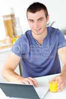 Charming young man using his laptop holding orange juice in the