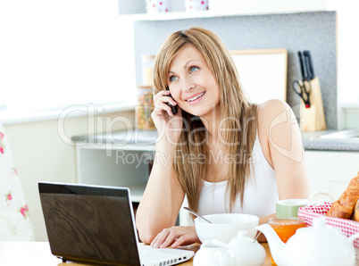 Young caucasian woman using her laptop and talking on phone duri