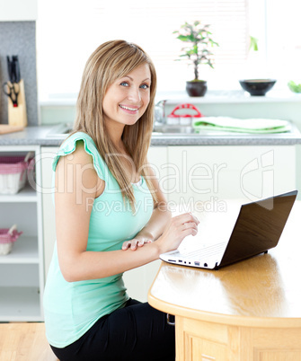 Delighted blond woman using her laptop smiling at the camera at