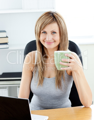 Glowing businesswoman holding a cup of coffee using her laptop a