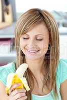 Smiling young woman holding a banana in the kitchen