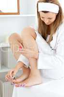 Attractive young woman varnishing her toenails in the bathroom